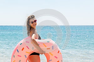 Beautiful sexy cute happy woman running on the beach with a pink rubber inflatable ring in the hand. Summer holidays and vacation