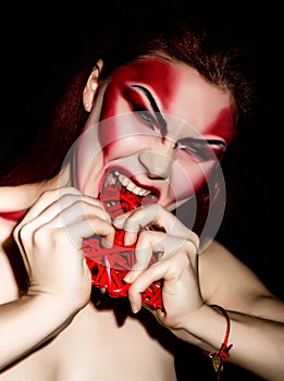 Beautiful devil girl with professional make-up. Fashion Art design. Attractive woman bites the heart