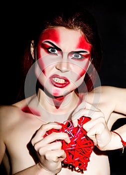 Beautiful devil girl with professional make-up. Fashion Art design. Attractive woman bites the heart