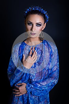 Beautiful elegant woman in a blue dress with a blue rim and design earrings in the studio on a black background