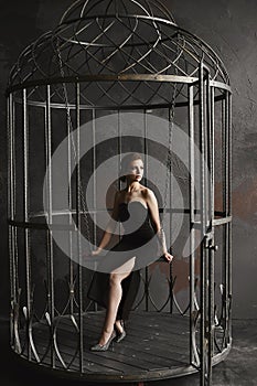 Beautiful, and fashionable brunette model girl in long black dress and bright silver shoes sits on a hanging swing and posing