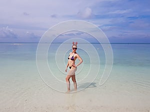 beautiful sexy fit woman in bikini and sunglasses standing in blue water on beach. Female wearing christmas reindeer headband