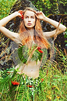 Beautiful girl Amazon with big lips is among the branches of fern in the woods on a summer day