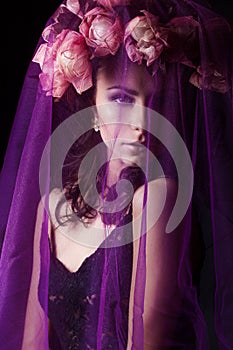 Beautiful girl with black hair in a black lace dress with a wreath on his head covered with a violet veil in the Studio