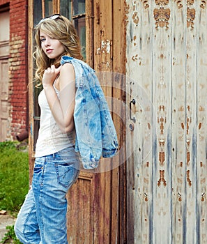 Beautiful girl blonde near an old abandoned house in sunglasses with large plump lips in jeans and a jacket