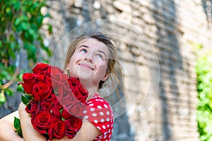 Beautiful and girl with a bouquet of red roses stands on the background of an old brick wall.