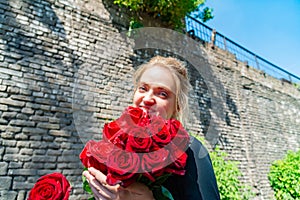 Beautiful and girl with a bouquet of red roses stands on the background of an old brick wall.