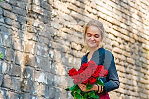 Beautiful and girl with a bouquet of red roses stands on the background of an old brick wall.