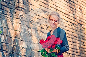 Beautiful and girl with a bouquet of red roses stands on the background of an old brick wall.
