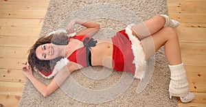 Beautiful girl with curly hair in Santa Claus clothes posing on warm rug