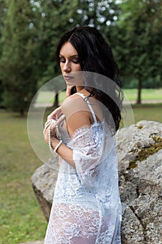 Beautiful girl with dark long hair in a light lace lingerie and negligee gown in nature summer warm evening