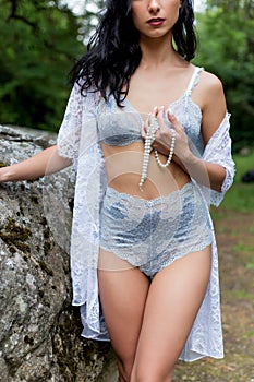 Beautiful girl with dark long hair in a light lace lingerie and negligee gown in nature summer warm evening