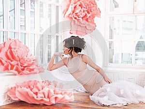 Beautiful girl in a long dress with a huge pink flowers sitting by the window