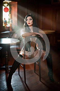 Beautiful girl with long leather boots sitting on chair in comfortable position. Brunette woman posing challenging