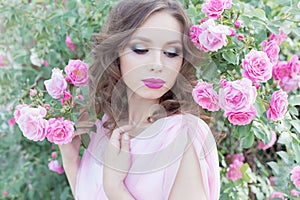 Beautiful girl in a pink dress standing in the garden roses in a sunny bright summer day with a gentle make-up and bright puf