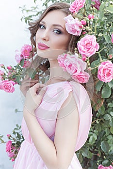 Beautiful girl in a pink dress standing in the garden roses in a sunny bright summer day with a gentle make-up and bright puf