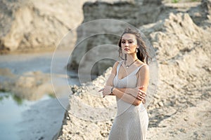 Beautiful sexy girl on the sea beach in a light dress looks at the camera, her hair fluttering in the wind at sunset