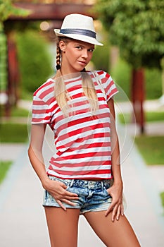 Beautiful girl in shorts and striped t-shirt, in hat, outdoors. Tanned girl in summer