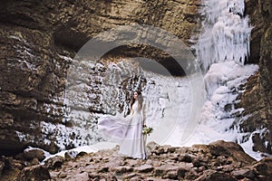 Beautiful girl in a wedding dress with a bouquet of flowers on a background of a glacier and mountains