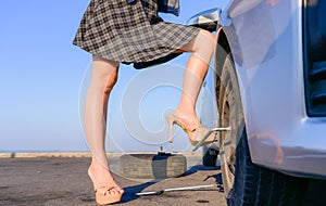 Beautiful sexy legs of woman treading on wrench while changing tire and wheel