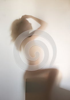 Beautiful and sexy long haired woman sits on block, poses behind a diffuse surface, behind a curtain.