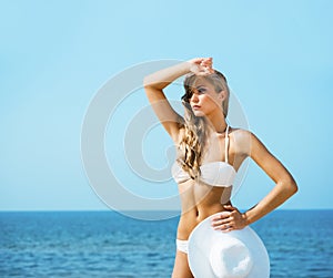 Beautiful, sexy, slim lady in alluring bikini posing with a hat