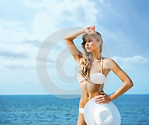 Beautiful, sexy, slim lady in alluring bikini posing with a hat