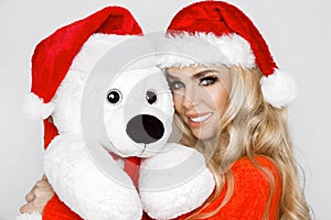 Beautiful sexy, smiling blonde model dressed in a Santa Claus hat, holding a teddy bear. Beauty sensual girl for Christmas