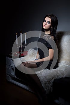 Beautiful sweet girl with full lips bright makeup sitting on the sofa with a glass of wine in a black evening dress