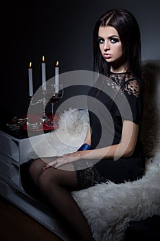 Beautiful sweet girl with full lips bright makeup sitting on the sofa with a glass of wine in a black evening dress