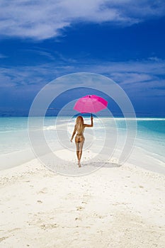 Beautiful sexy tanned woman bikini model with pink umbrella on Maldives island. Young glamour girl in swimsuit on Maldives