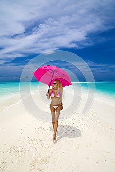 Beautiful sexy tanned woman bikini model with pink umbrella on Maldives island. Young glamour girl in swimsuit on Maldives