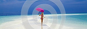 Beautiful sexy tanned woman bikini model with pink umbrella on Maldives island. Young glamour girl in swimsuit on Maldives