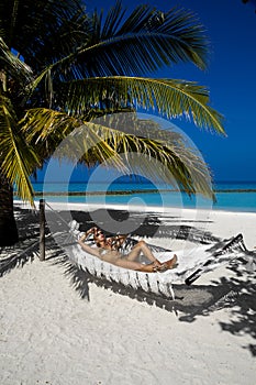 Beautiful sexy tanned woman in golden bikini on Maldives island. Young glamour girl is posing on hammock in paradise . Perfect