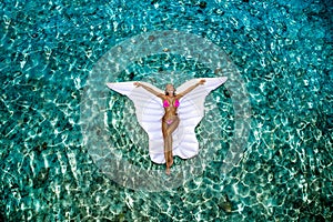 Beautiful sexy tanned woman on white butterfly mattress in pool. Young glamour girl in swimsuit on Maldives island. Perfect body