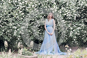 Beautiful tender blonde girl in blue light dress with a sprig of jasmine in his hands sitting the garden in the style