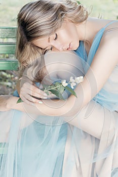 Beautiful tender blonde girl in blue light dress with a sprig of jasmine in his hands sitting the garden in the style