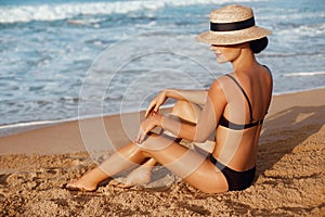 Beautiful Sexy Woman in bikini apply sun protection cream on her smooth tanned legs. Skin care. Legs on the beach