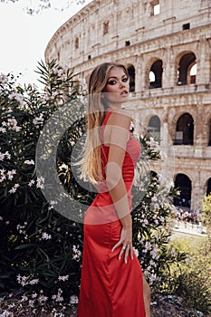 beautiful sexy woman with blond hair in elegant red dress posing near Colloseum