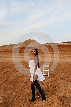 Beautiful sexy woman with dark hair in elegant clothes and accessories posing in desert