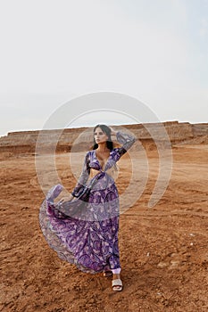 Beautiful sexy woman with dark hair in elegant dress and accessories posing in desert