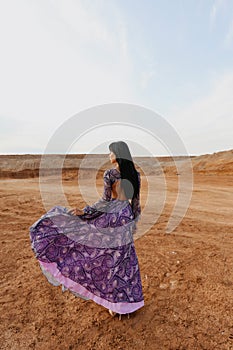 Beautiful sexy woman with dark hair in elegant dress and accessories posing in desert