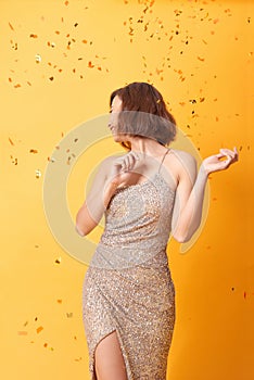 Beautiful sexy woman in evening dress celebrating, golden confetti, party, smiling, inviting, happy