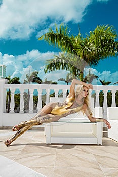 Beautiful sexy woman in gold bikini and gold shoes posing on the caribbean luxury hotel