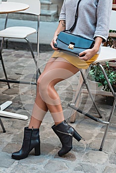 beautiful sexy woman with long smooth legs in yellow skirt ankle botie and with a hand bag clutch