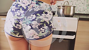 Beautiful Sexy woman Sport Booty in short shorts dancing in the kitchen and cooks food in a skillet