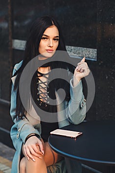 Beautiful sexy woman in stylish fashionable dress and coat. Fashion girl posing at coffee shop outdoors