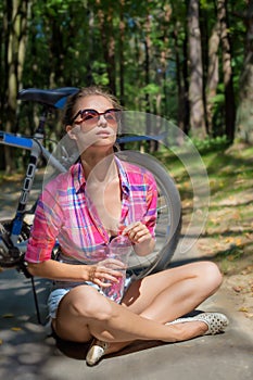 Beautiful woman in sunglasses in the woods drinking water near bicycle