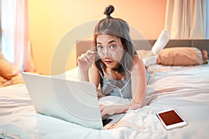 Beautiful and sexy woman using laptop computer and listening to music from cell phone on bed