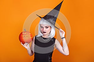 Beautiful sexy woman in witch hat and costume holding carved pumpkin. Happy halloween